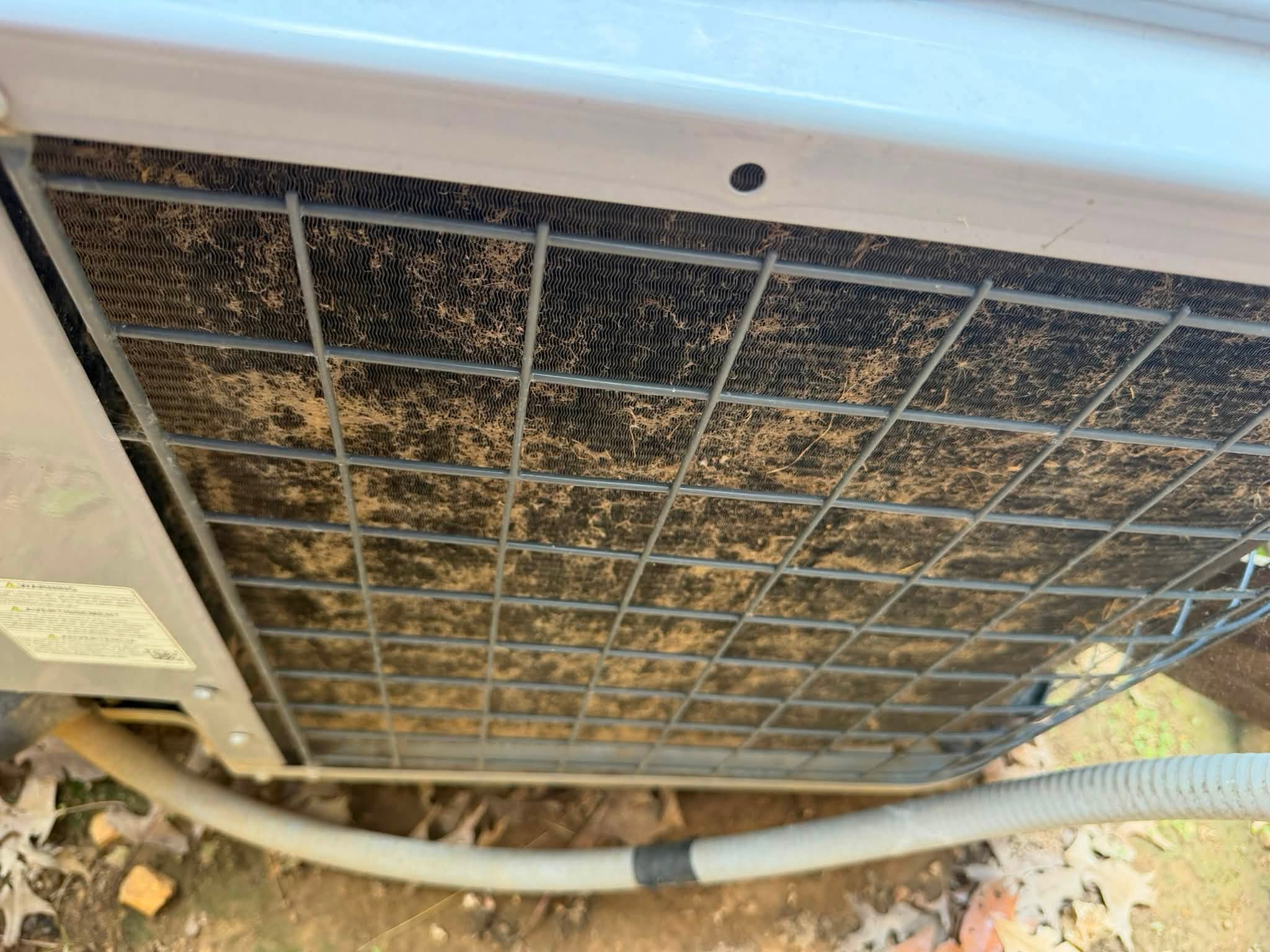 Close-up of debris accumulated on an outdoor AC coil before maintenance
